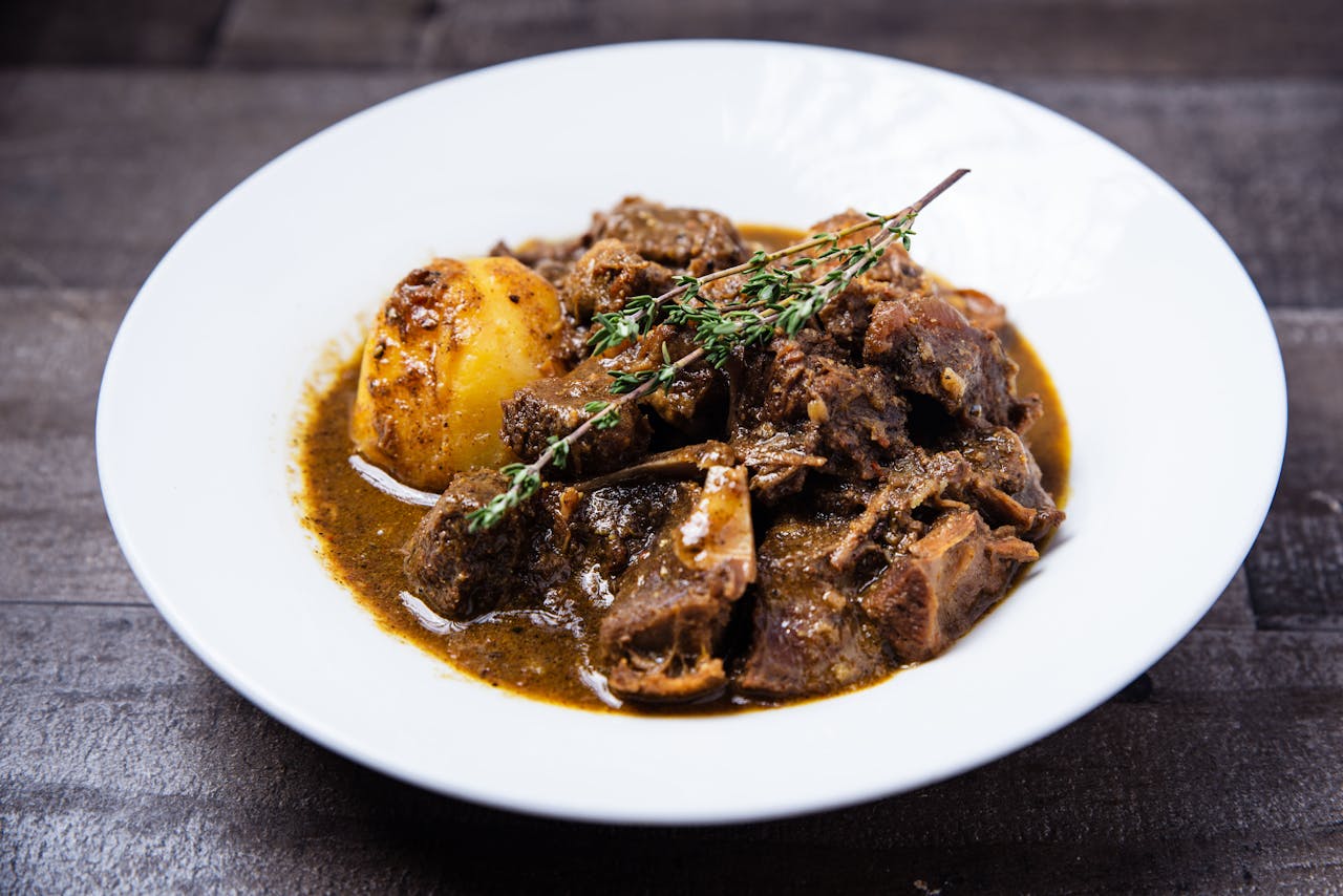 Close-up of savory Caribbean oxtail stew with potatoes served on a white plate.