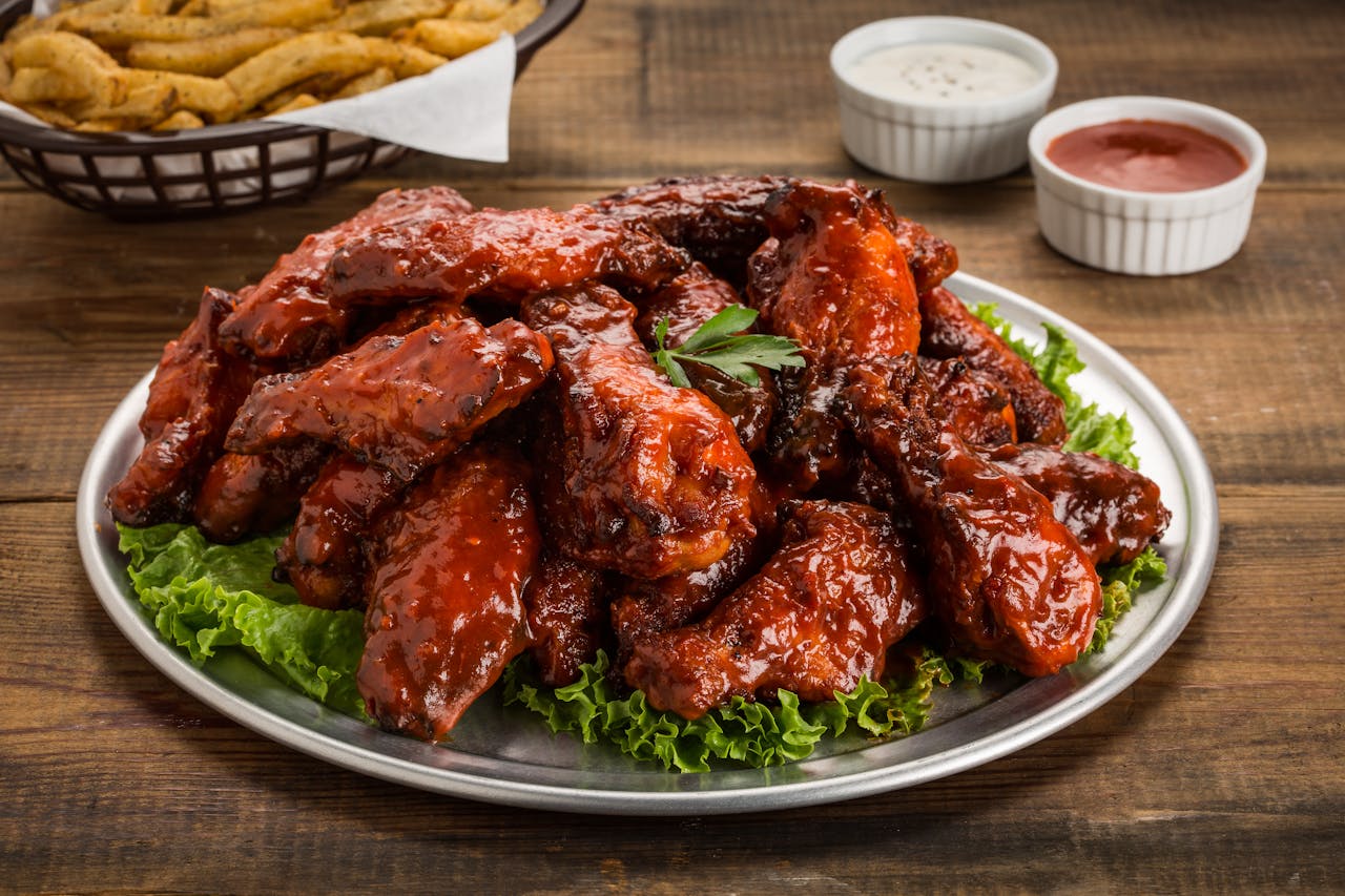 Tasty BBQ chicken wings served with green lettuce and dipping sauces on a wooden table.